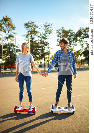 Young man and woman riding on the Hoverboard in the park. content technologies. a new movement. Young man and woman riding on the Hoverboard in the park. content technologies. a new movement. 103671487