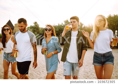 Group of friends cheers and drink beers on the beach. Young friends relaxing and having picnic. Suummertime. 103672305