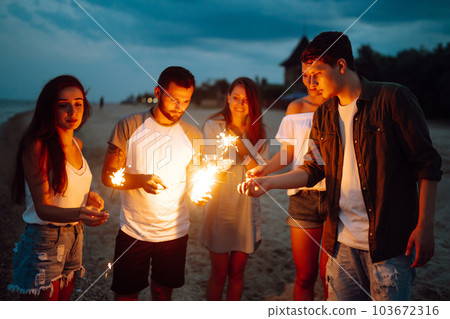 Group of people holding sparklers at party on the beach. Young friends have fun with fire sparkles. Group of people holding sparklers at party on the beach. Young friends have fun with fire sparkles. 103672316