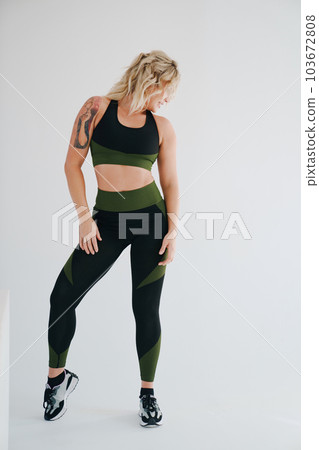 an attractive blonde in a black and green tracksuit poses on a white background. 103672808
