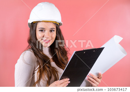 Smiling woman architect wearing white hardhat and and delighted expression enjoys job Smiling woman architect wearing white hardhat and and delighted expression enjoys job 103673417