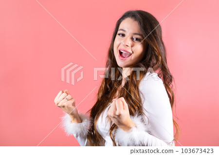 Young woman showing funny dance moves enjoys party. Brown-haired lady smiles happily with life at pink wall studio 103673423