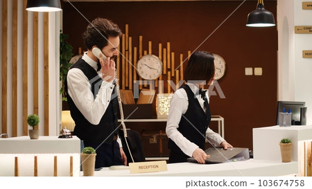 Teamworking professional hotel personnel checking tourists reservation date at check in reception desk. Receptionists coworkers discussing incoming guests booking informations Teamworking professional hotel personnel checking tourists reservation date at check in reception desk. Receptionists coworkers discussing incoming guests booking informations 103674758