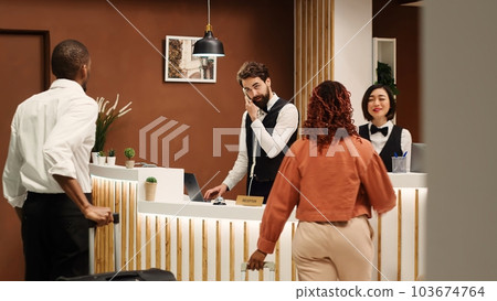Professional concierge personnel welcoming tourists at reception desk during check in process. Elegant friendly receptionist team greeting vacation trip guests in hotel lobby Professional concierge personnel welcoming tourists at reception desk during check in process. Elegant friendly receptionist team greeting vacation trip guests in hotel lobby 103674764