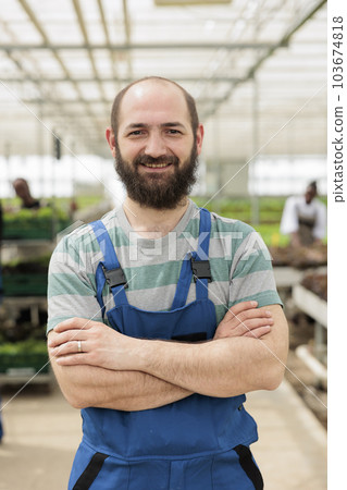 Agricultural farm worker proudly standing in front of naturally grown nutritious vegan food crops produced locally and sustainably in chemical free environmentally conscious greenhouse 103674818