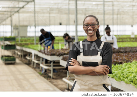 Happy smiling entrepreneur ranch manager leading group of farmers harvesting locally non-GMO eco friendly food crops. Sustainable bio agriculture in certified organic greenhouse. 103674854