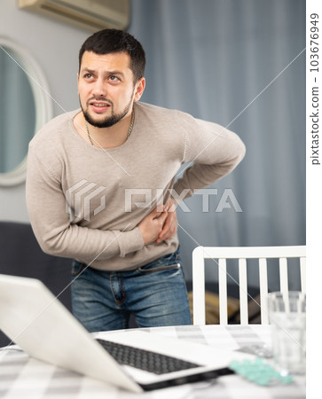 Man experiences severe pain in his side, the fruit of prolonged work on laptop at home 103676949