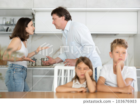 Brother and sister sit at table during quarrel between parents 103676983