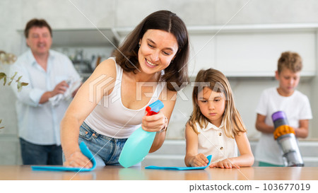 Positive mother and daughter cleaning the surface of kitchen table 103677019