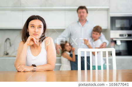 Offended wife sits at table and listens as her husband yells at her 103677041