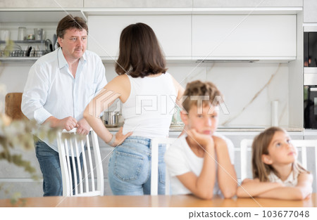 Angry parents quarrelling in the kitchen and children sitting at the table Angry parents quarrelling in the kitchen and children sitting at the table 103677048