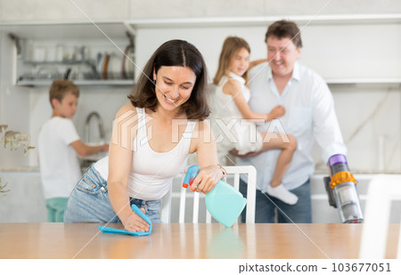 Positive mother cleaning the surface of kitchen table Positive mother cleaning the surface of kitchen table 103677051