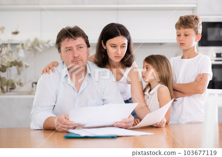 Wistful father looking through papers with family Wistful father looking through papers with family 103677119