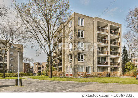 an apartment building on the corner of a street with cars parked in front and trees lining the road behind it 103678323