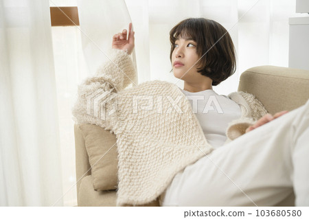 Young woman looking out through the gap in the curtains 103680580