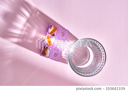 Bright pill box with different pills and vitamins next to a glass of water. 103681339