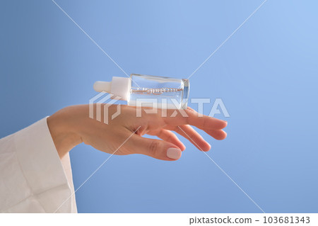 Serum with a pipette in female hands on a blue background. Serum with a pipette in female hands on a blue background. 103681343