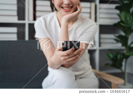 Young relaxed smiling pretty woman relaxing sitting on sofa at home. Female feeling joy enjoying with mobile phone on cozy couch 103681617