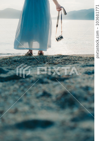 Photo of a woman standing with a camera at the beach 103681771