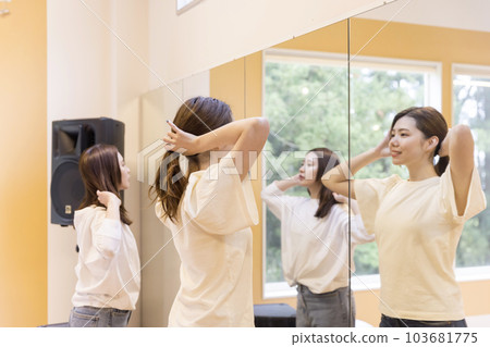 Young woman tying her hair in front of a mirror in a lesson studio 103681775