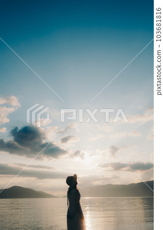 Photo of a silhouette woman standing with a camera at the beach Photo of a silhouette woman standing with a camera at the beach 103681816