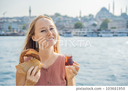 Woman in Istanbul having breakfast with Simit and a glass of Turkish tea. Glass of Turkish tea and bagel Simit against golden horn bay in Istanbul, Turkey. Turkiye 103681950
