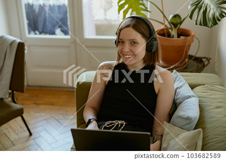 Smiling woman using laptop for online learning or watching movie while lying on sofa at home 103682589