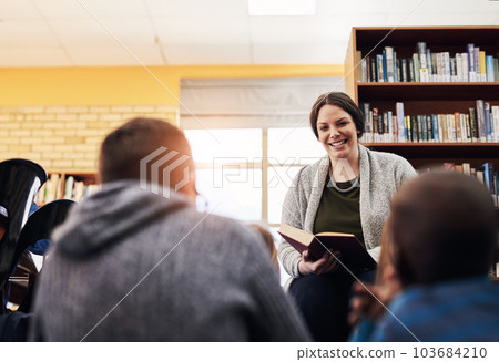 Theyre always looking forward to story time. an elementary schoolteacher reading a book to her students in the library. 103684210