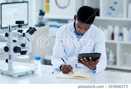 The research is paying off. a focused young male scientist browsing on a digital tablet while making notes inside of a laboratory. 103686373
