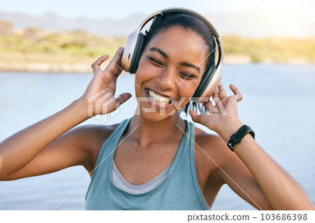 Excited woman smiling and listening to music with water in the background. Happy young female enjoying tunes on her online streaming playlist while outdoors. Using wireless headphones play songs Excited woman smiling and listening to music with water in the background. Happy young female enjoying tunes on her online streaming playlist while outdoors. Using wireless headphones play songs 103686398