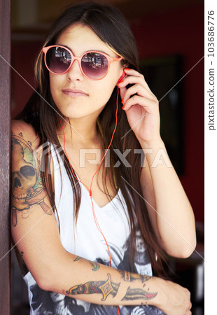 Tattoo, earphones and punk gen z woman with urban fashion or style relax while listening to music online. Podcast, radio and unique female person streaming audio or rock in summer with freedom 103686776