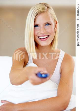 Changing channels. A young woman sitting in front of the television pointing the remote at you. 103686827