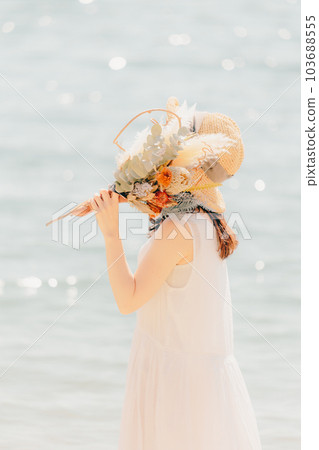 A woman standing with dried flowers on the beach A woman standing with dried flowers on the beach 103688555
