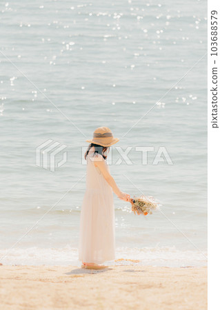 A woman standing with dried flowers on the beach A woman standing with dried flowers on the beach 103688579