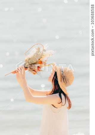 A woman standing with dried flowers on the beach A woman standing with dried flowers on the beach 103688588