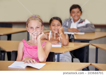Portrait, kids and smile of student in classroom with book, ready to learn and study in class. Group of students, education and girl learning in primary school for knowledge, development or studying. 103688701