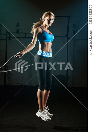 Woman, jump rope and fitness in gym, energy and action with healthy, active person. Portrait, young female athlete and exercise with performance, cardio workout and health with sports in gymnasium 103688895