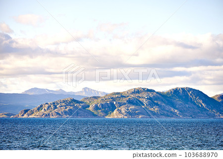 Scenic view of sea, mountains, rocks and boulders in Norway. Tidal ocean water waves, blue sky with clouds and copy space. Travel and tourism overseas and abroad to a remote and peaceful destination 103688970