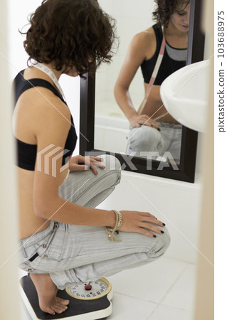 Anorexia, diet and woman with a scale, weight loss and wellness in the bathroom, nutrition and fitness. Female person, model and girl with mirror, measure and body care with health issue and problem 103688975