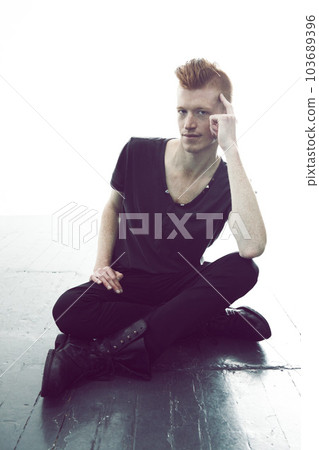 Portrait, ginger and man sitting on a floor with hand on head or wearing black or in thought for fashion and against white wall. Mohawk, dark and young guy thinking in punk clothes or rock and roll Portrait, ginger and man sitting on a floor with hand on head or wearing black or in thought for fashion and against white wall. Mohawk, dark and young guy thinking in punk clothes or rock and roll 103689396