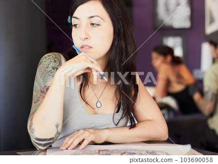 Thinking, tattoo shop and woman artist with drawing for body art, design and creativity in ink parlor. Tattoos, idea and serious female person with pencil in thoughtful, contemplating and wonder face Thinking, tattoo shop and woman artist with drawing for body art, design and creativity in ink parlor. Tattoos, idea and serious female person with pencil in thoughtful, contemplating and wonder face 103690058