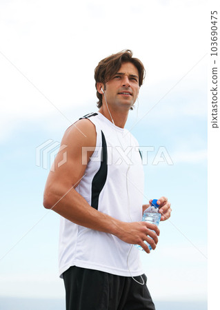 He has a strong motivation for physical fitness. Handsome young male holding a water bottle, listening to music and looking away after his morning run. 103690475