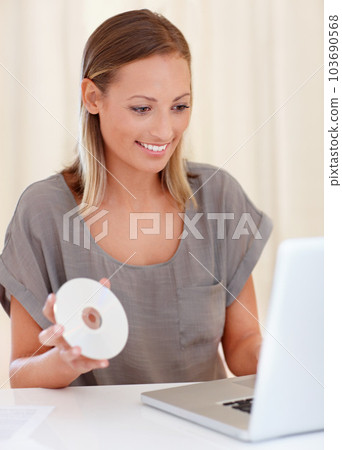 Shes been waiting for this program. A young woman sitting in front of her laptop and holding a disc. Shes been waiting for this program. A young woman sitting in front of her laptop and holding a disc. 103690568