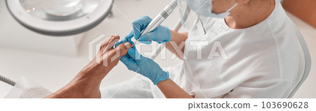 Lady uses grinding machine to polish toenail of male client at in beauty salon Lady uses grinding machine to polish toenail of male client at in beauty salon 103690628