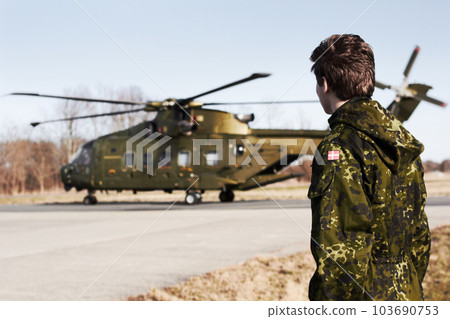 Army, military or soldier man with a helicopter outdoor for transportation, Denmark war and pilot mission. Male person for combat, flight or air force service in camouflage uniform to watch or patrol 103690753