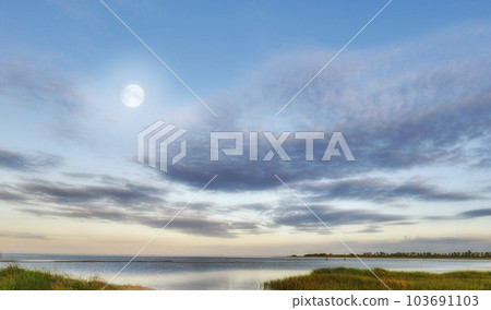 Nature landscape of a cloudy blue sky over the ocean waters. Winter sunrise views on empty calm beach at low tide. Beautiful seaside scene of the natural, peaceful and stressless outdoors. 103691103