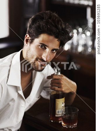 Man, pub counter and portrait with drink at happy hour with alcohol and whiskey after work. Bottle, male person and face of a handsome guy with a glass and style and confidence in a luxury bar Man, pub counter and portrait with drink at happy hour with alcohol and whiskey after work. Bottle, male person and face of a handsome guy with a glass and style and confidence in a luxury bar 103691285