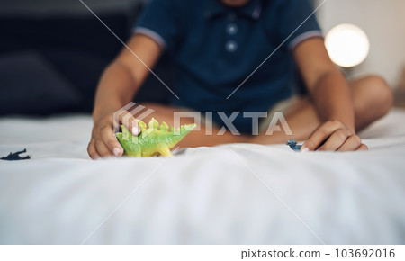 Dinosaurs are his favourite animals. an unrecognizable boy playing with dinosaurs while sitting on his bed. Dinosaurs are his favourite animals. an unrecognizable boy playing with dinosaurs while sitting on his bed. 103692016