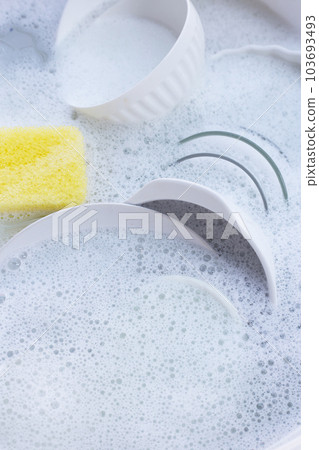 Dishes and bowls with yellow sponge in water and bubbles of dishwashing liquid 103693493
