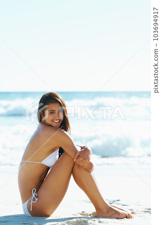 Shes a cute beach babe. A gorgeous young woman sitting on the beach. Shes a cute beach babe. A gorgeous young woman sitting on the beach. 103694917